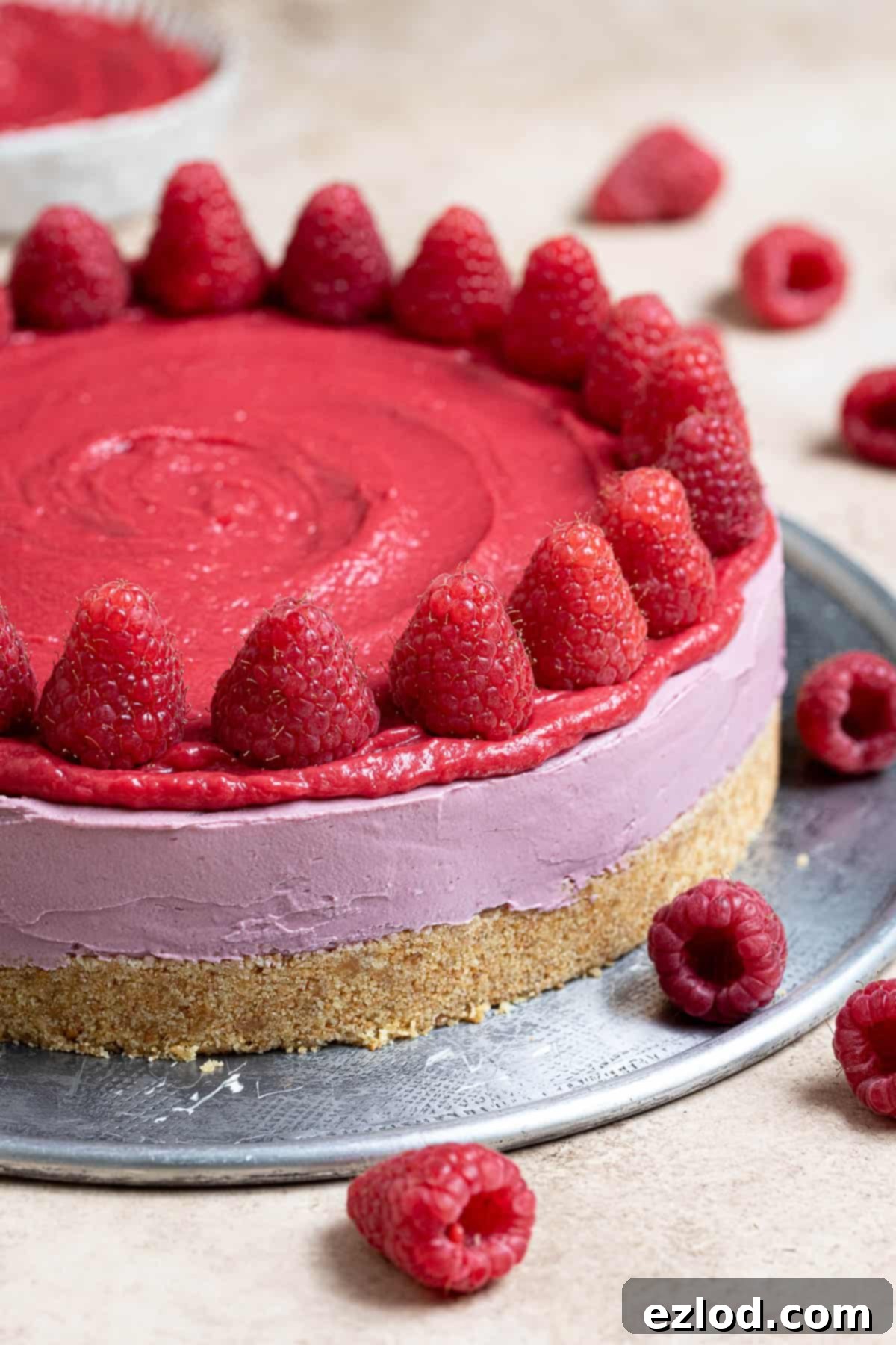 A stunning vegan raspberry cheesecake, elegantly topped with fresh raspberries, presented on a chic metal plate. Its vibrant colors promise a delicious experience.