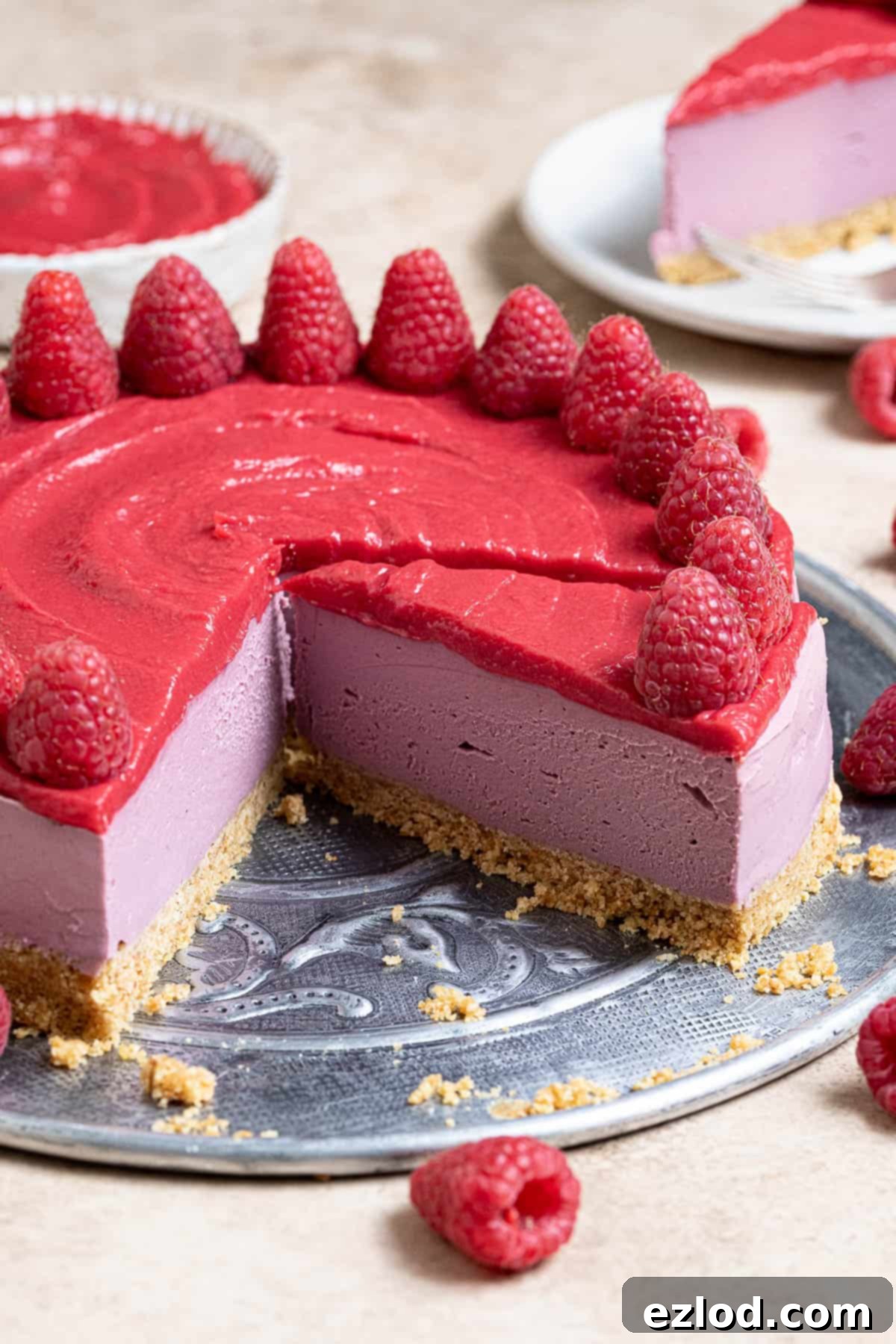 A stunningly presented vegan raspberry cheesecake, professionally sliced and artfully arranged on a sleek metal plate, inviting indulgence.