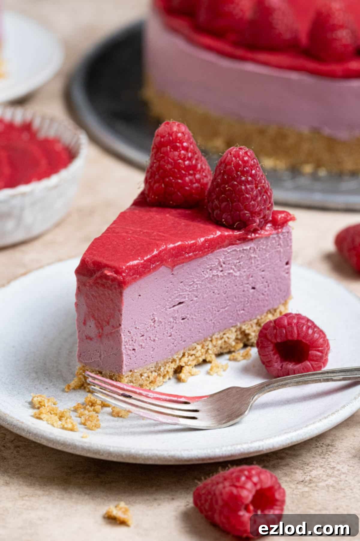 An enticing close-up of a slice of vegan raspberry cheesecake, positioned on a white plate with a forkful already savored, highlighting its creamy texture.