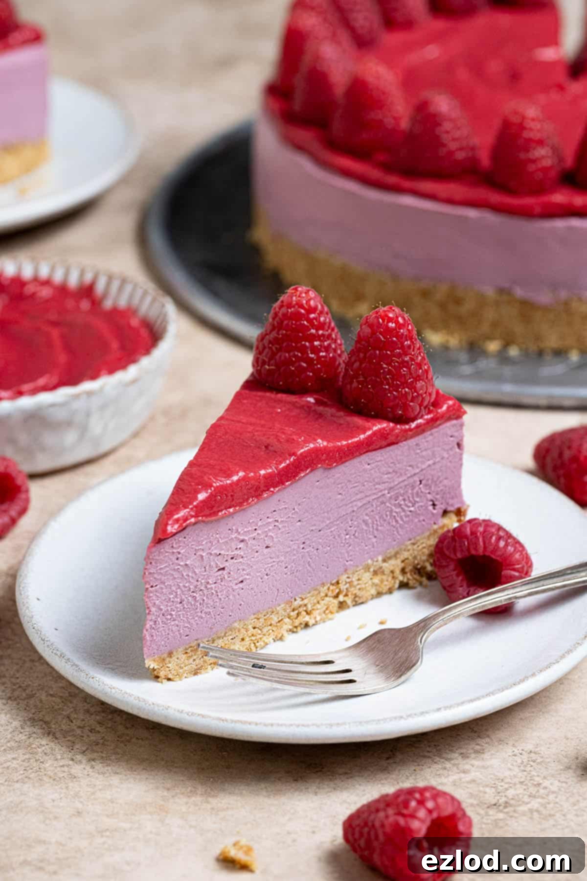 A perfectly sliced piece of vegan raspberry cheesecake, showcasing its creamy layers and crumbly base, served on a pristine white plate.