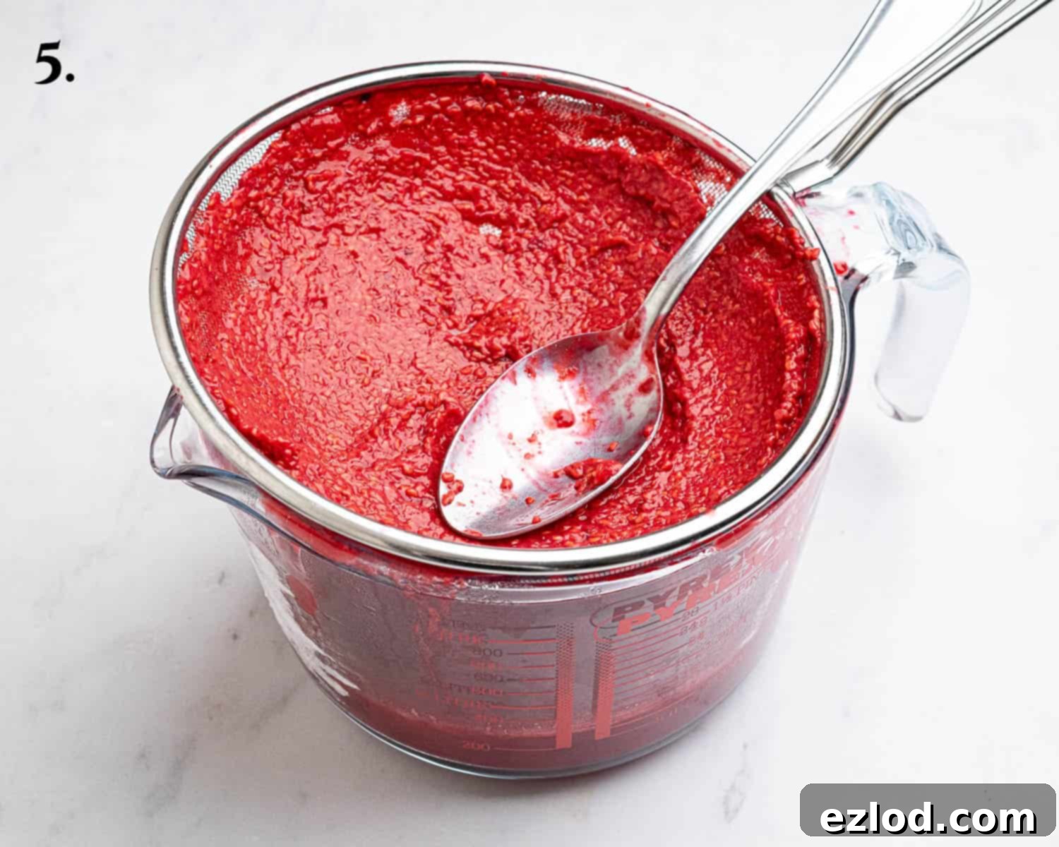 Step 5, the process of pressing raspberry puree through a fine mesh sieve to remove seeds, ensuring a smooth filling.
