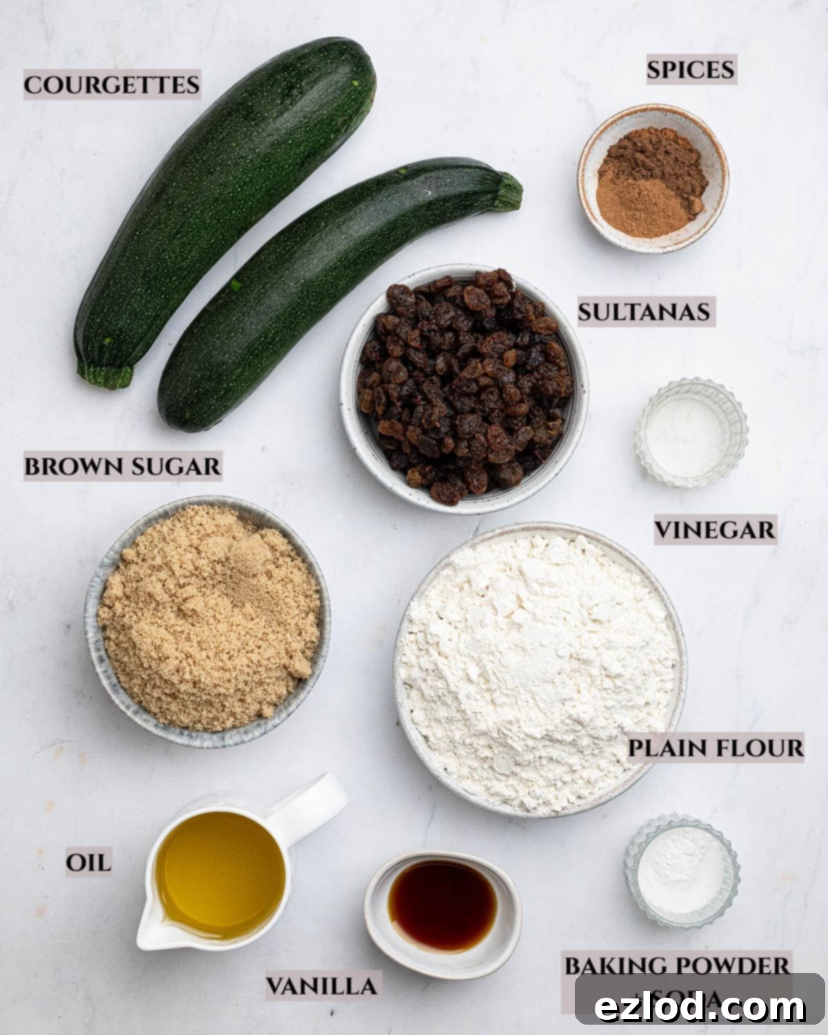 Vegan Zucchini Spice Cake 3 A labelled photo of the essential ingredients needed to make spiced courgette cake, including fresh courgettes, flour, light brown sugar, neutral oil, and various warm spices.
