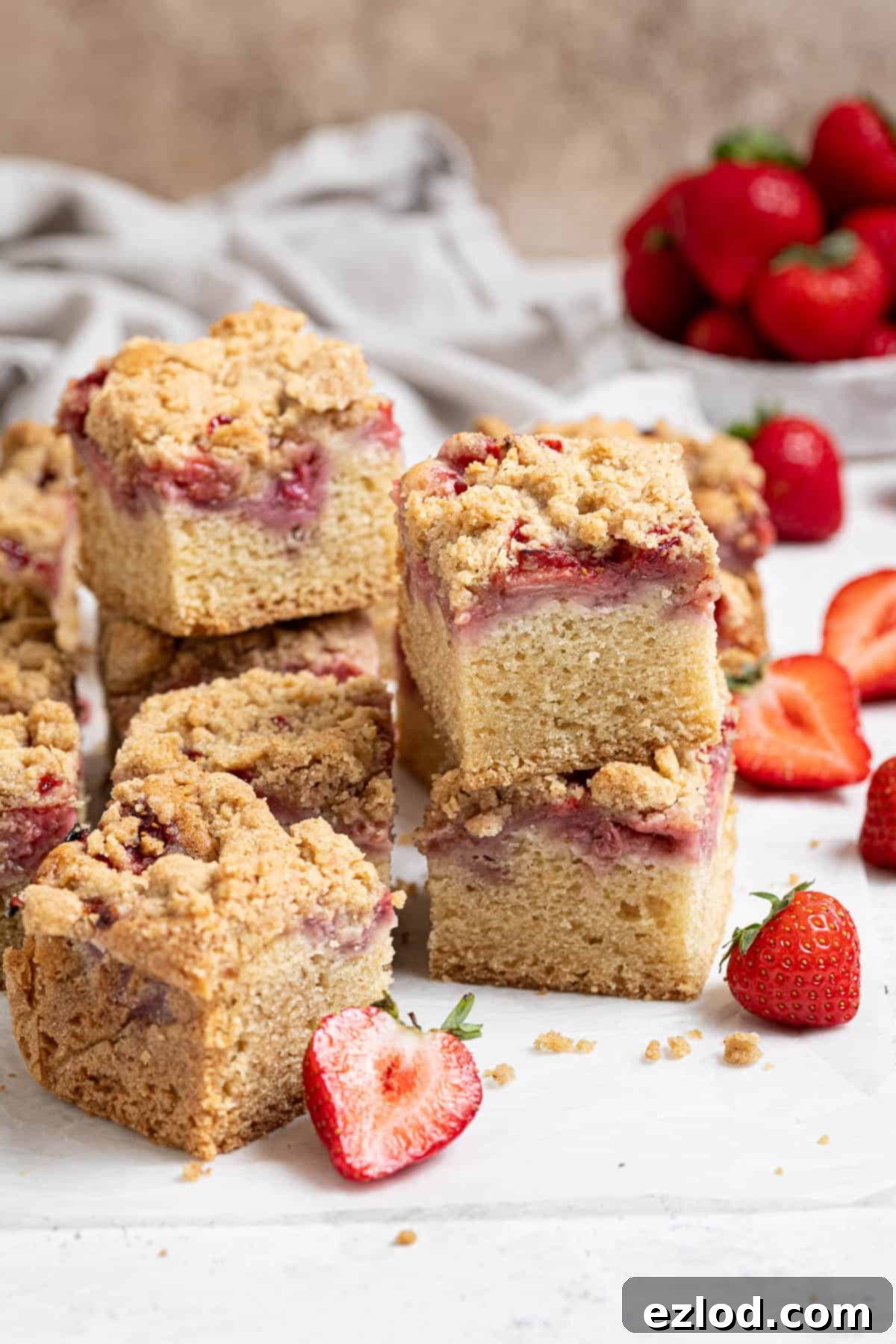 Vegan Strawberry Crumb Cake 13 Stacks of delicious vegan strawberry crumb cake squares with a bowl of fresh strawberries in the blurred background.