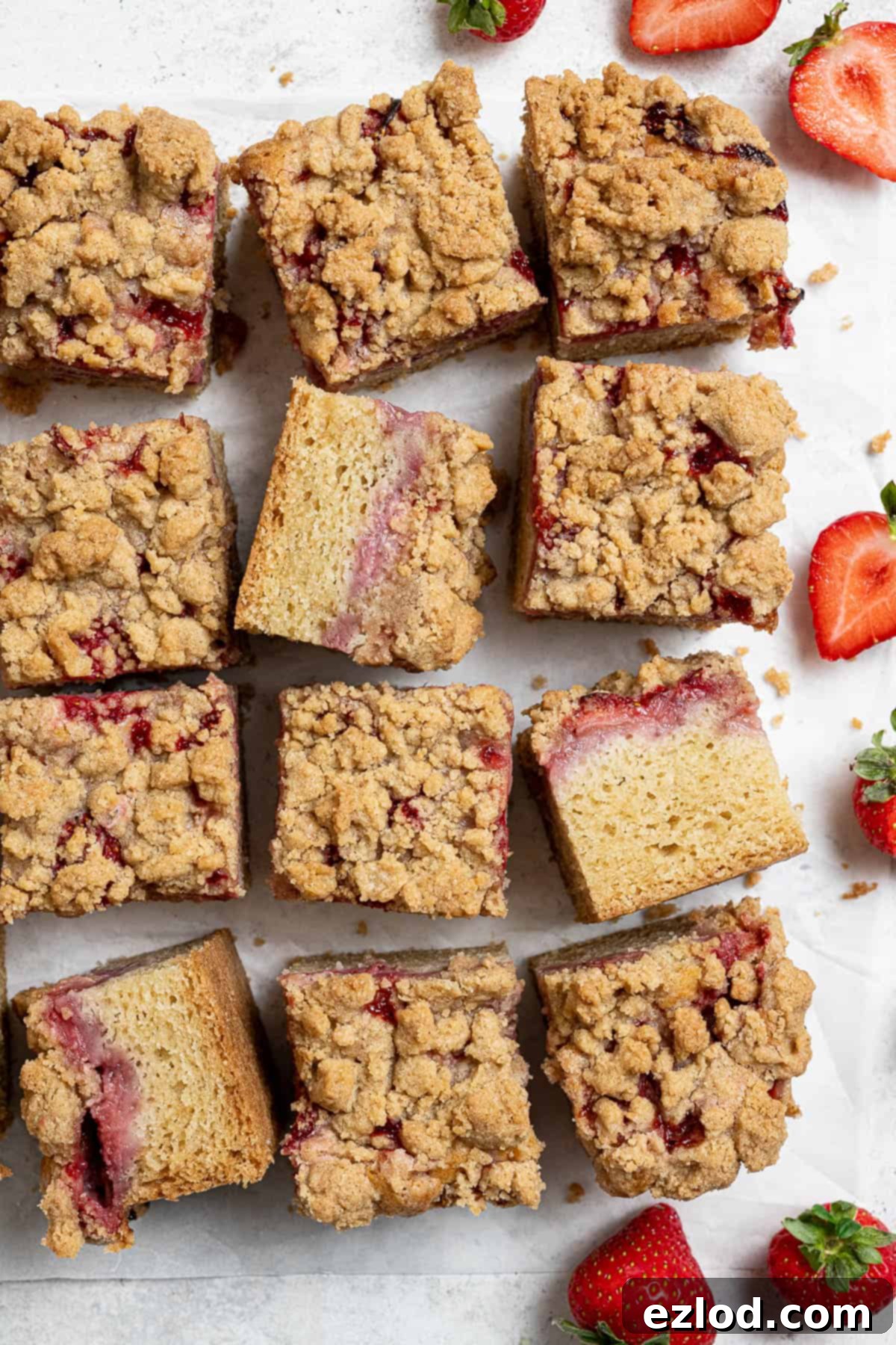 Vegan Strawberry Crumb Cake 4 Squares of vegan strawberry crumb cake arranged on a white background with fresh strawberries beside them.