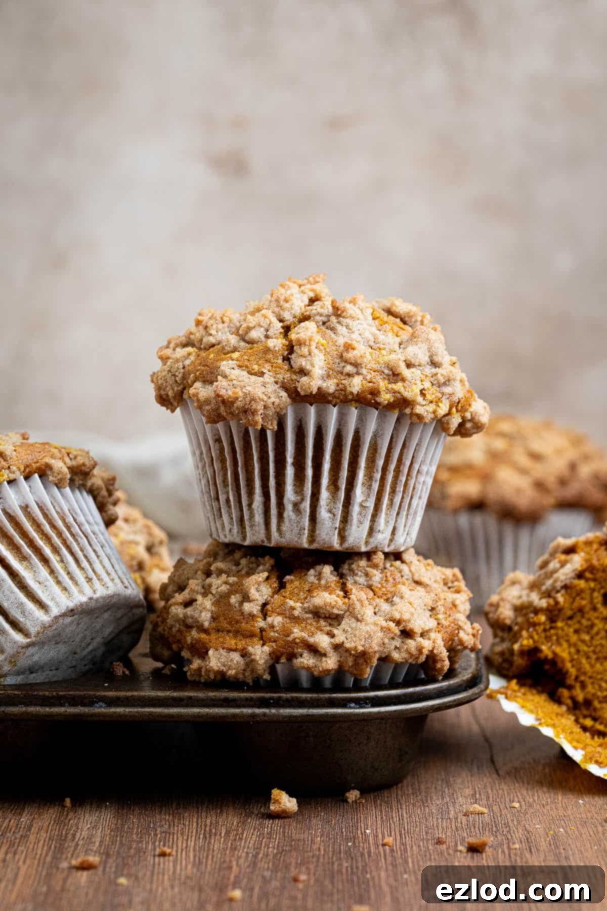 A stack of two vegan pumpkin streusel muffins in a muffin tin, showcasing their tall tops and streusel.