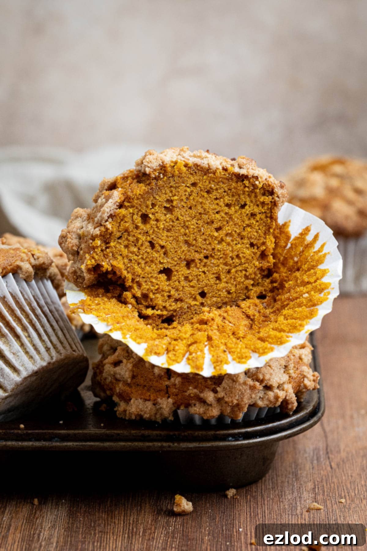 A perfectly baked vegan pumpkin muffin, sliced in half to reveal its tender crumb, resting on a muffin tin.