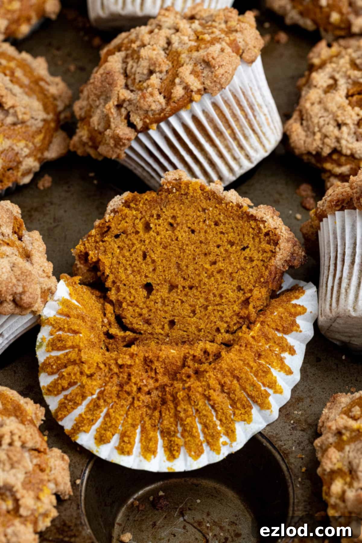 A vegan pumpkin streusel muffin sliced in half, showing its moist interior and crunchy topping, placed on a muffin tin.