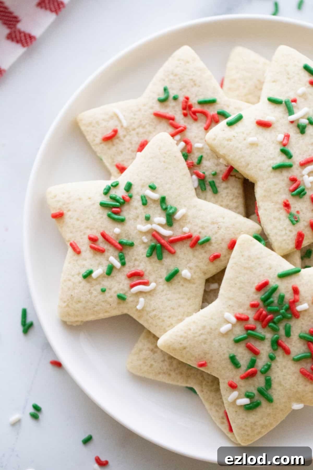 A white round plate with a stack of festive gluten free star shaped sugar cookies adorned with Christmas colored sprinkles.