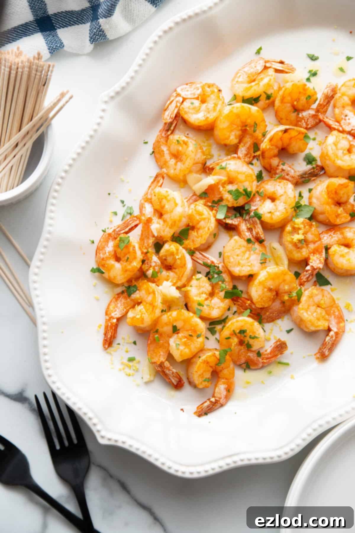 Festive platter of cooked shrimp with toothpicks and pretty matte black forks nearby.