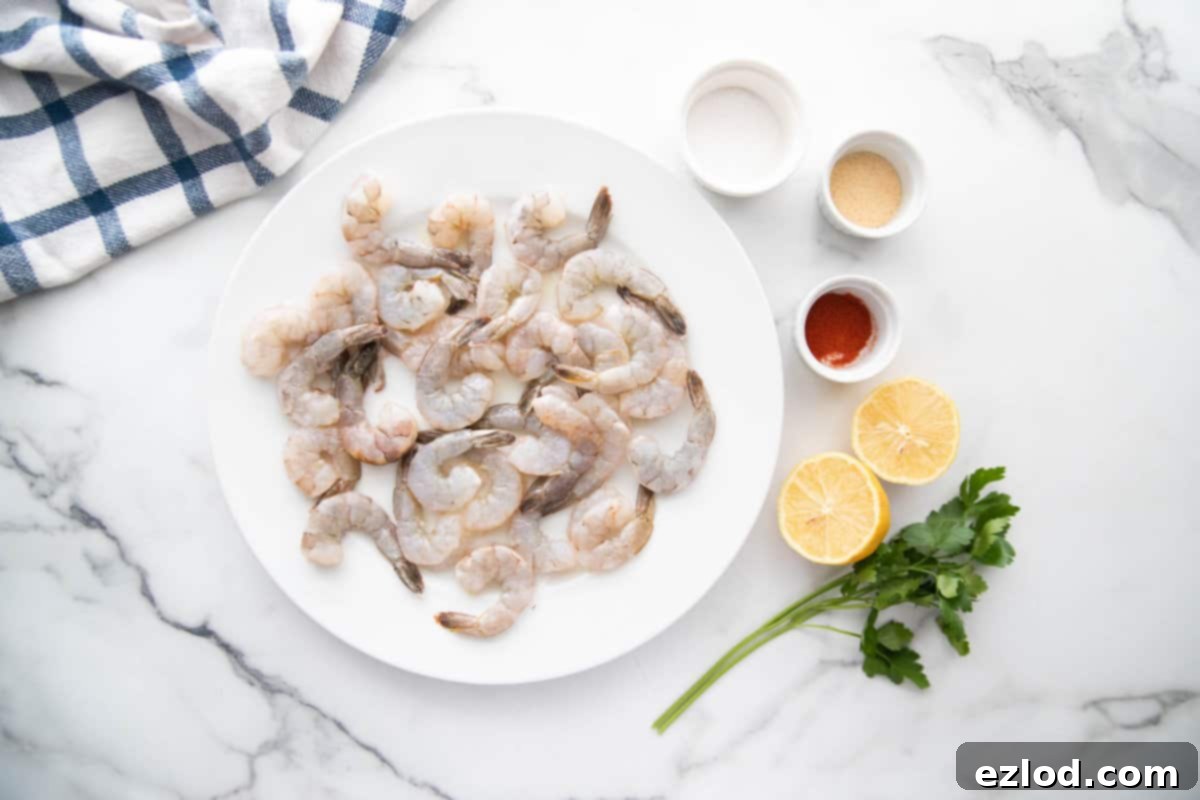 Raw shrimp with the tail on next to seasonings, lemon, and fresh parsley.