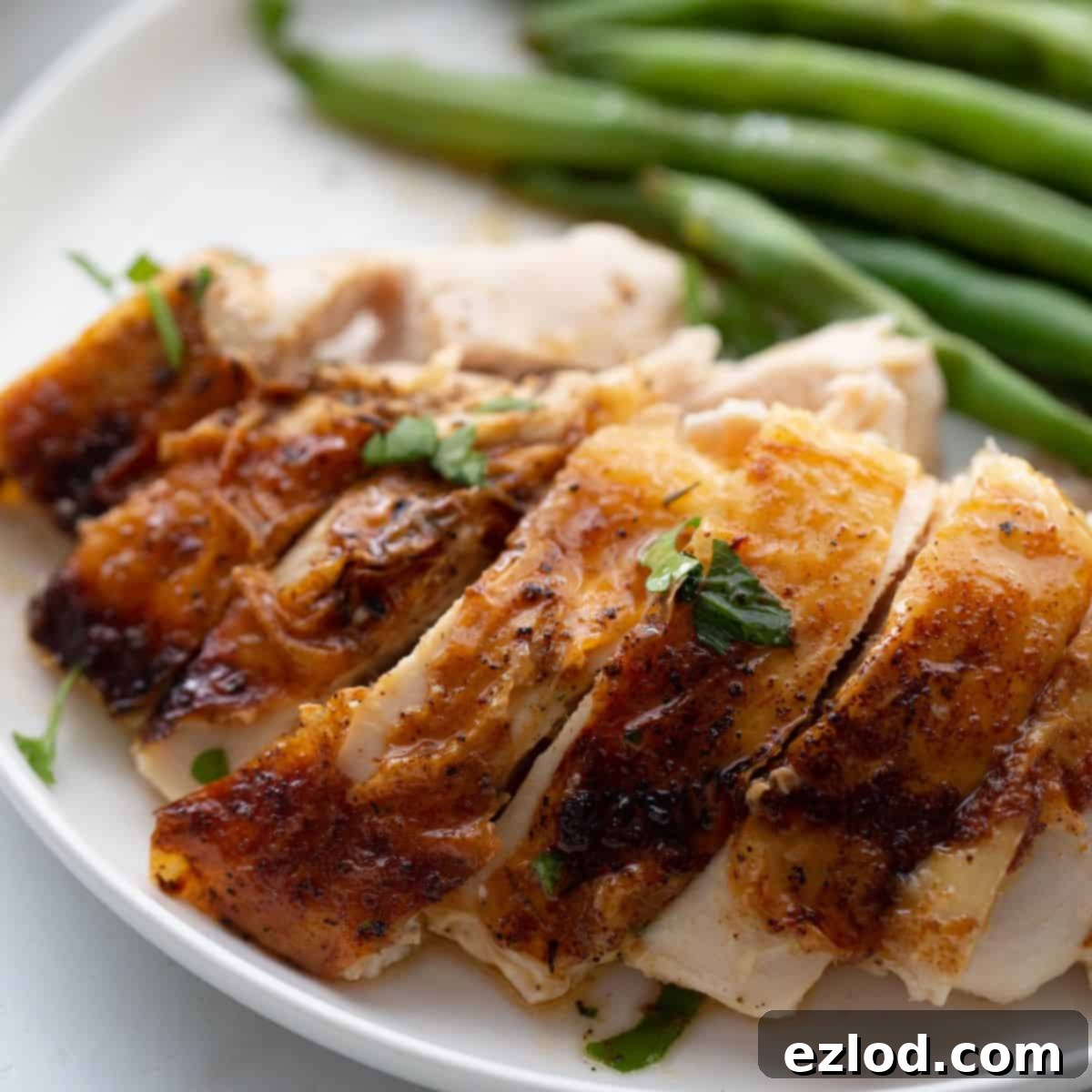 Sliced air fryer whole chicken on a white plate with a side of vibrant green beans, showcasing its golden, crispy skin and succulent interior.