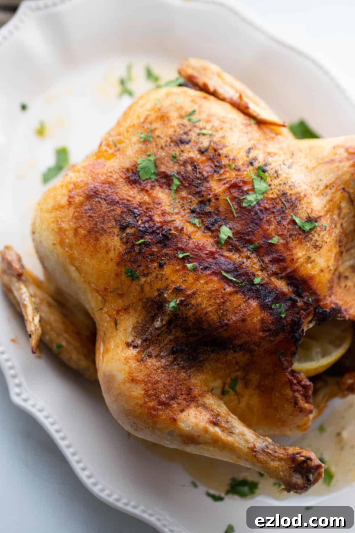An beautifully air fryer roasted whole chicken resting on a pristine white platter, garnished and ready for carving.