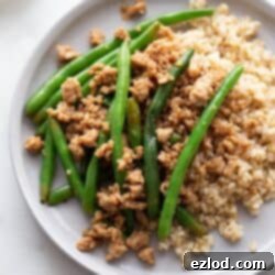 A plate of ground chicken stir fry on a bed of brown rice and stopped with steamed green beans.