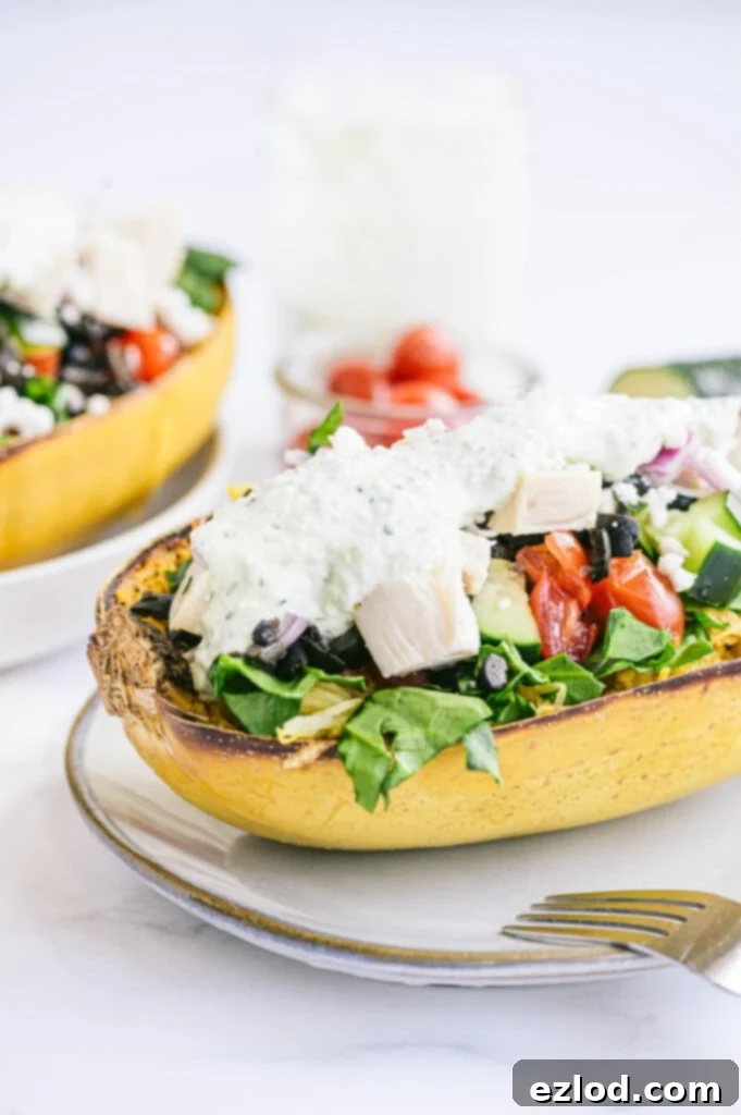 Half of a roasted spaghetti squash generously stuffed with a vibrant mix of chicken, Mediterranean vegetables, and a dollop of creamy homemade Tzatziki sauce, ready to be enjoyed.