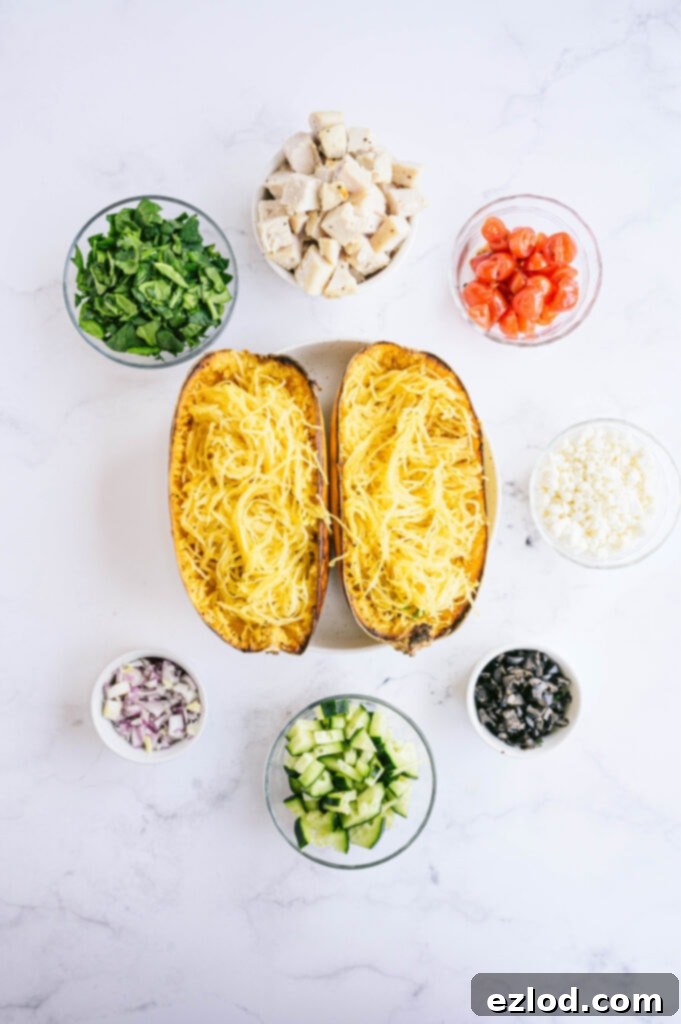 An inviting overhead photo displaying a roasted spaghetti squash alongside an array of Mediterranean-inspired toppings artfully arranged in glass bowls, including chicken, feta, tomatoes, and olives.