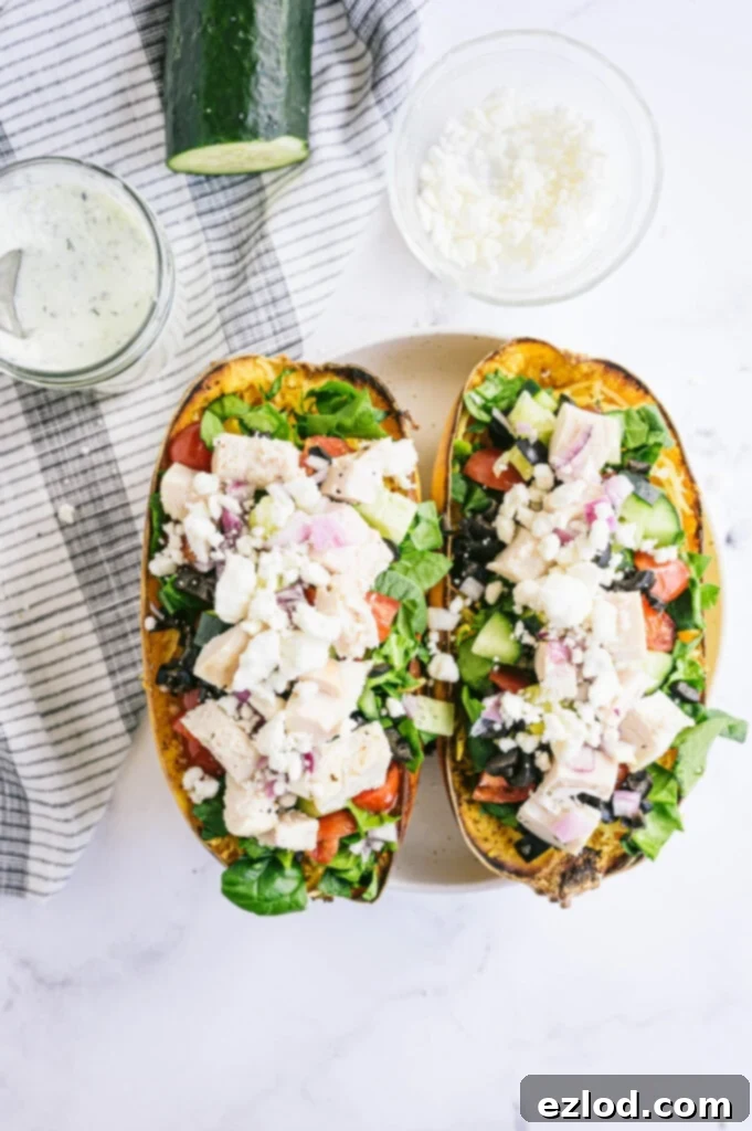 A visually stunning close-up of a spaghetti squash half, generously loaded with vibrant Mediterranean vegetables and diced chicken, crowned with crumbled feta cheese. A side dish of creamy homemade Tzatziki sauce completes the appetizing scene.