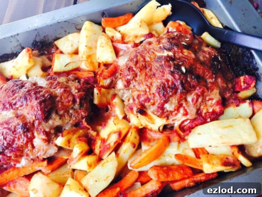 A metal baking pan displaying two perfectly cooked meatloaves, each glistening with savory tomato sauce and topped with crispy, bubbly cheese. Roasted carrots and potatoes are arranged on either side, ready to be served. A black serving spoon rests nearby, inviting diners to dish up this wholesome Momma's Meatloaf.