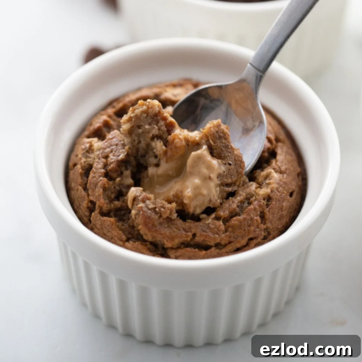 Baked oatmeal in a white ramekin with someone spooning out a bite with melty peanut butter baked inside.