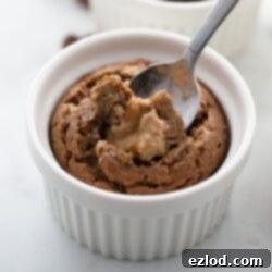 Baked oatmeal in a white ramekin with someone spooning out a bite with melty peanut butter baked inside.