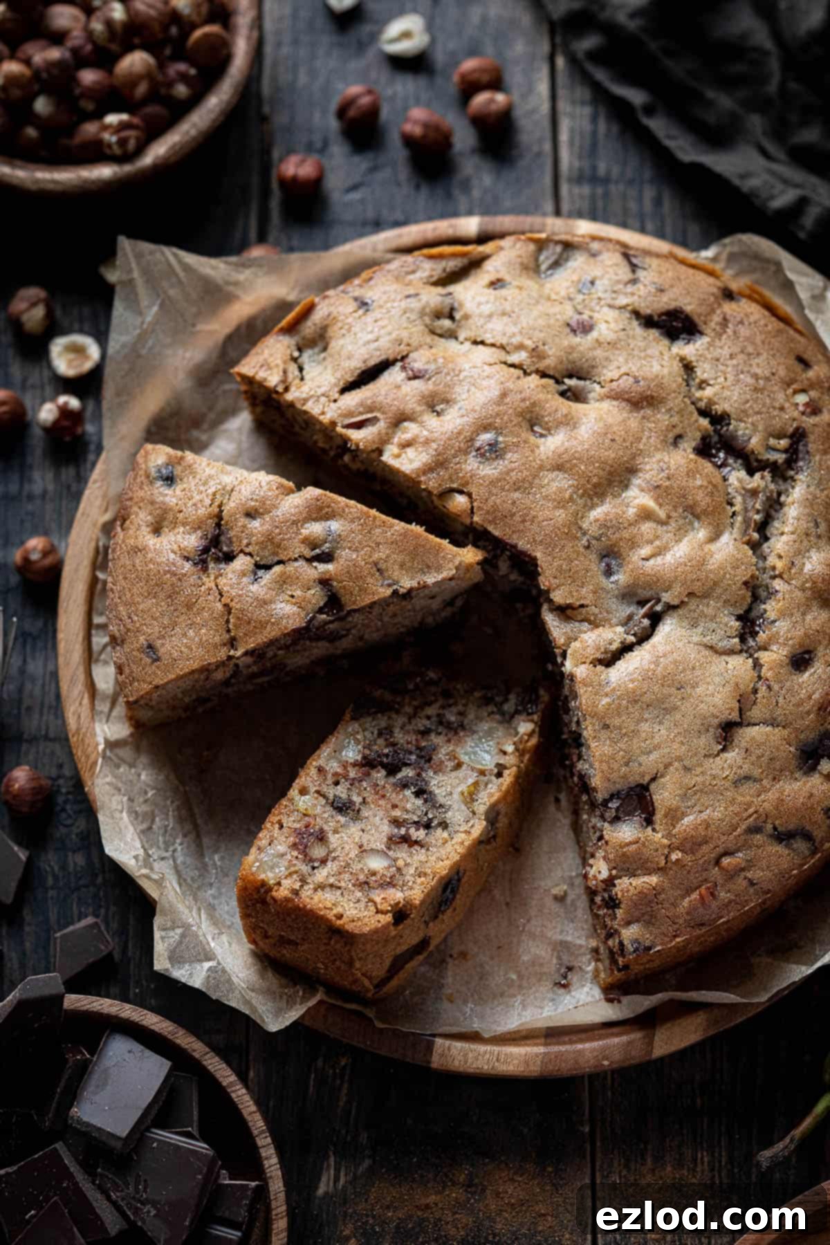 A close-up, top-down shot of a freshly baked chocolate, pear, and hazelnut cake, perfectly sliced, revealing the golden crumb and generous distribution of ingredients.
