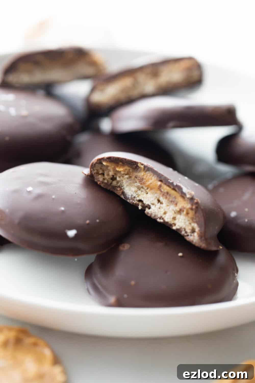 Close-up of a plate of homemade Tagalongs, with one cookie thoughtfully bitten into, clearly exposing the crispy oat flour cookie and a thick, inviting layer of creamy peanut butter beneath the perfectly set chocolate coating.