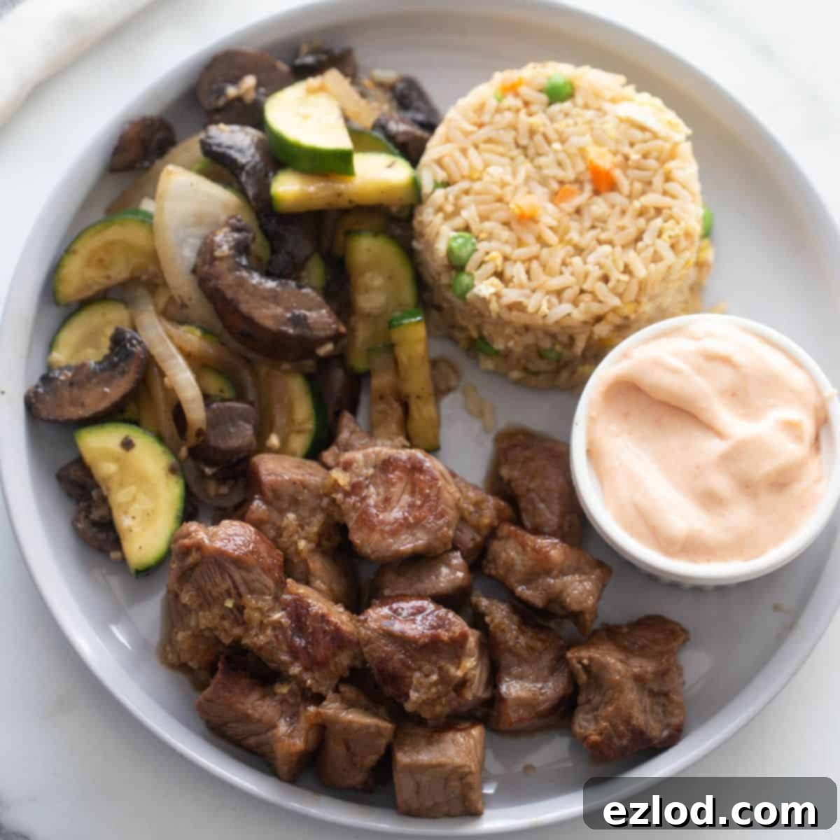Sizzling Hibachi Steak 2 White plate with hibachi steak, hibachi veggies, yum yum sauce, and fried rice.