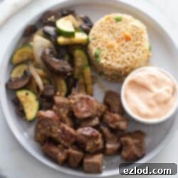 Sizzling Hibachi Steak 8 White plate with hibachi steak, hibachi veggies, yum yum sauce, and fried rice.
