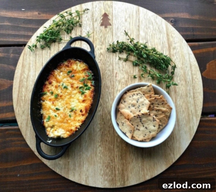 Cast iron pan of baked feta dip next to a white bowl of gluten free crackers on a wooden round, garnished with thyme. Close-up of the bubbly, golden-brown roasted feta.