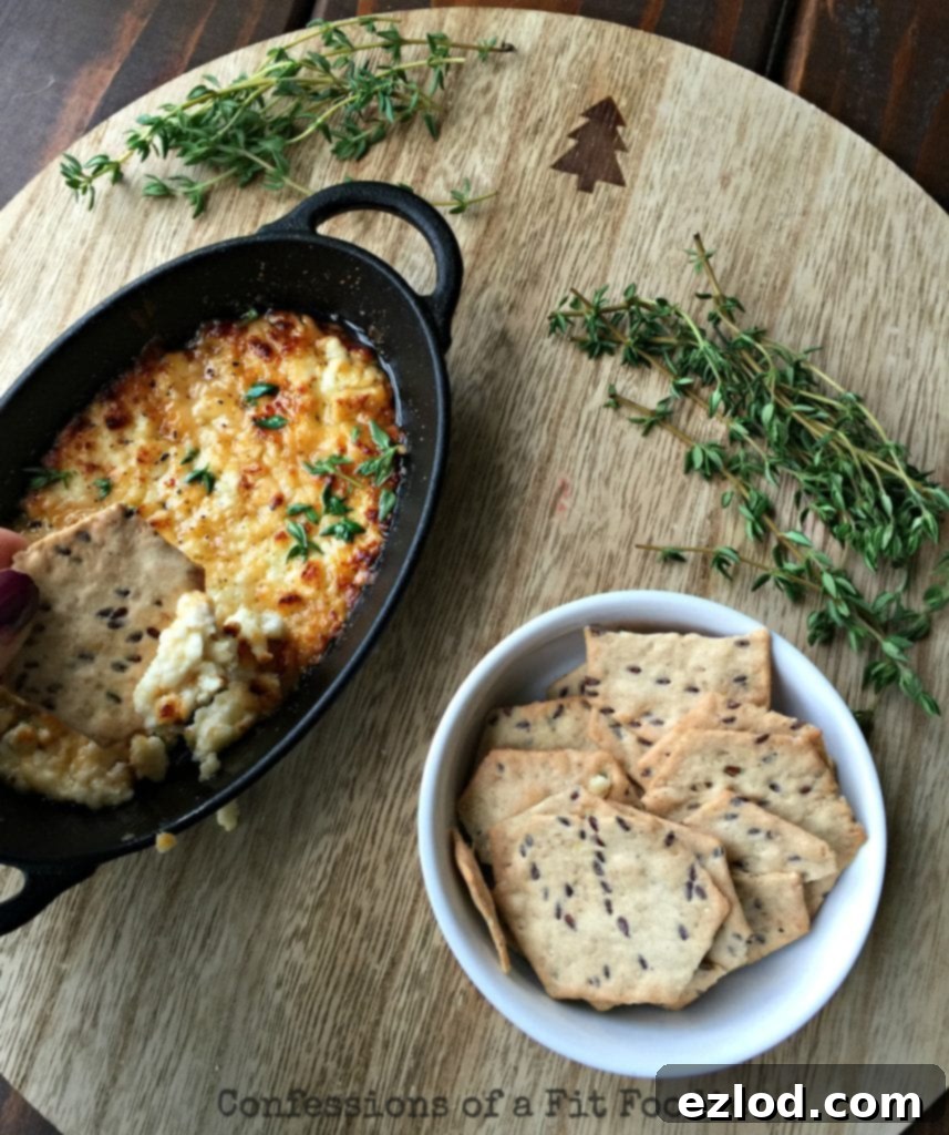 Close up photo of warm, golden roasted feta dip with gluten free crackers on a rustic wooden background, highlighting the creamy texture.