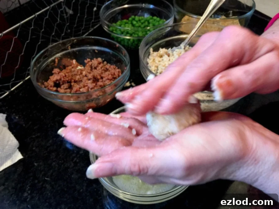Hands in the process of rolling a Mini Arancini Rice Ball, with bowls of prepared ingredients visible in the background, illustrating the hands-on creation.