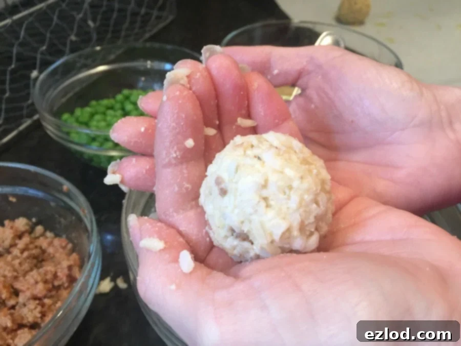 A woman's hands hold a perfectly formed Mini Arancini Rice Ball, ready for the next step of dipping in breading, showcasing its smooth, rounded shape.