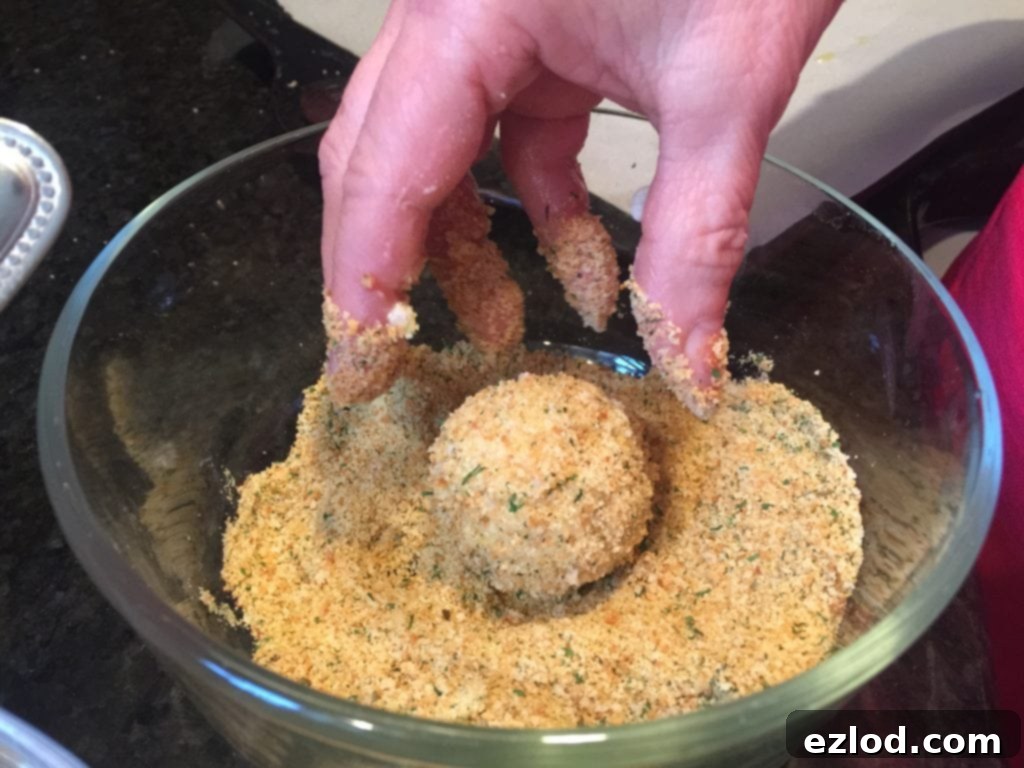 A freshly coated Mini Arancini Rice Ball rests in a bowl of gluten-free breadcrumbs, ready for baking.