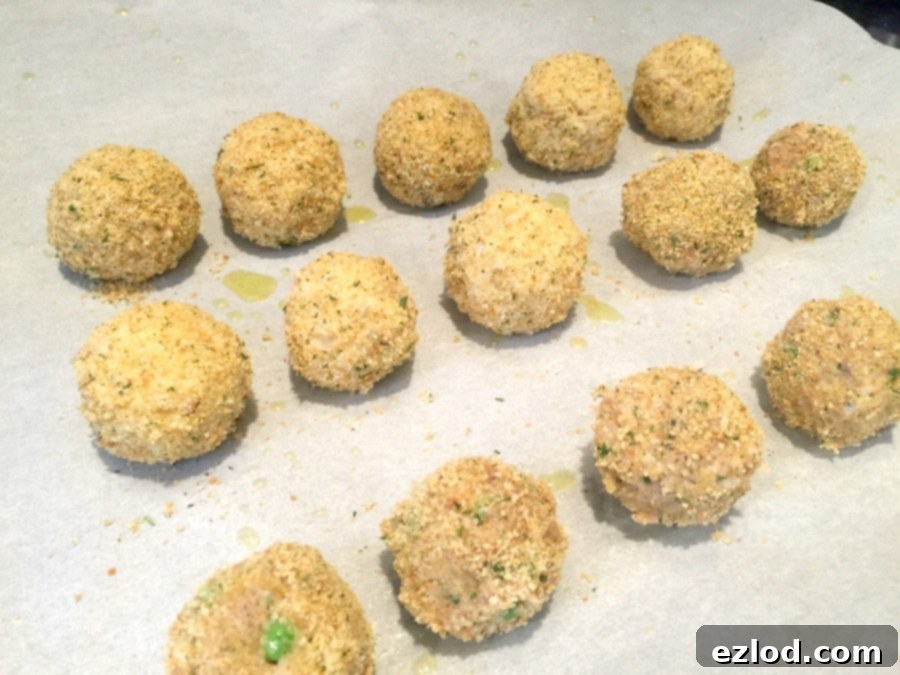 Rows of unbaked Mini Arancini Rice Balls, perfectly breaded and ready for the oven on a parchment-lined baking sheet.