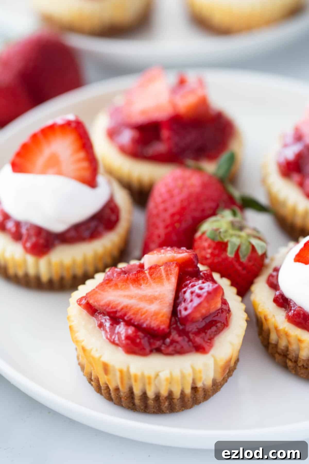 Close up image of Healthy Mini Cheesecakes with strawberry topping on a white plate. The ones in front are in focus, and the ones at the top of the image are out of focus.