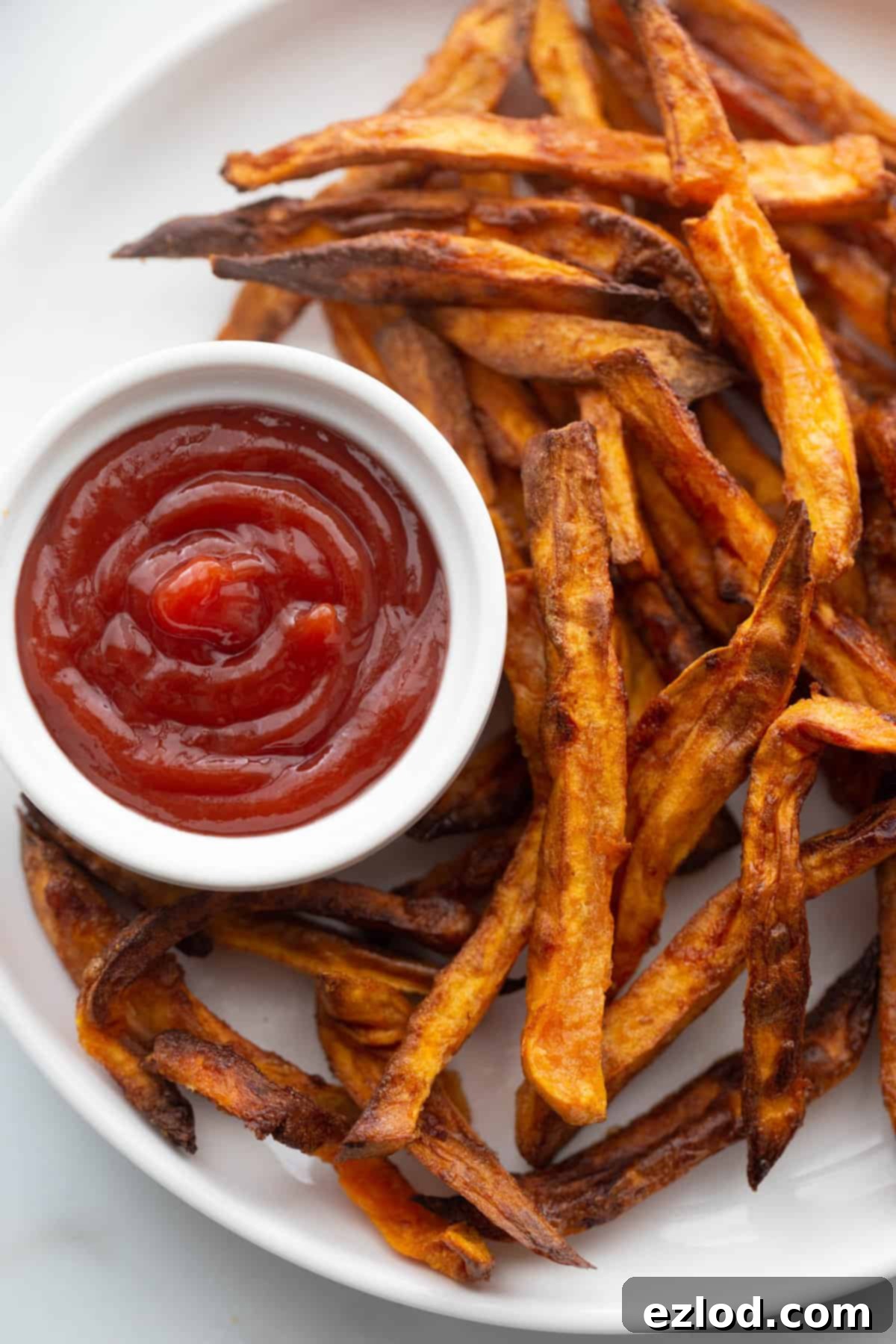 Perfectly Crispy Air Fryer Sweet Potato Fries 3 Homemade sweet potato fries on a white plate with a side of ketchup.