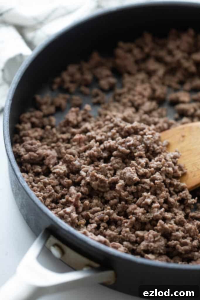 A large skillet with cooked group beef and a wooden spoon.