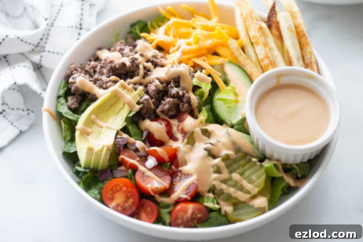 Burger bowl with ground beef, tomatoes, pickles, lettuce, sliced avocado, fries, and a side of special sauce.