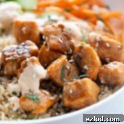 Bowl of sticky air fryer salmon bites over brown rice with spicy mayo sesame seeds and cilantro.