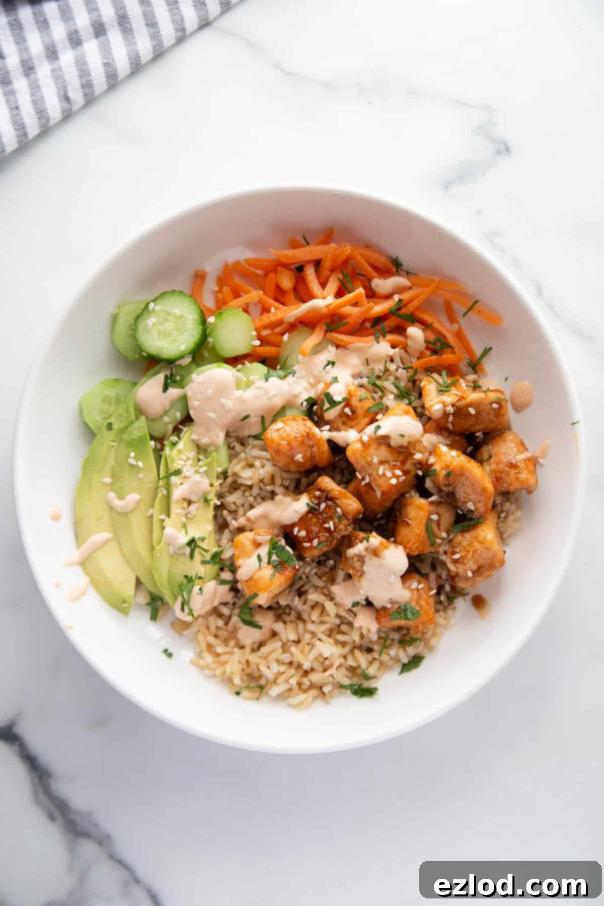 A beautifully presented bowl of sticky air fryer salmon bites, served over a mix of brown rice and fresh vegetables, topped with creamy spicy mayo, a scattering of sesame seeds, and vibrant cilantro, alongside sliced avocado for extra richness.