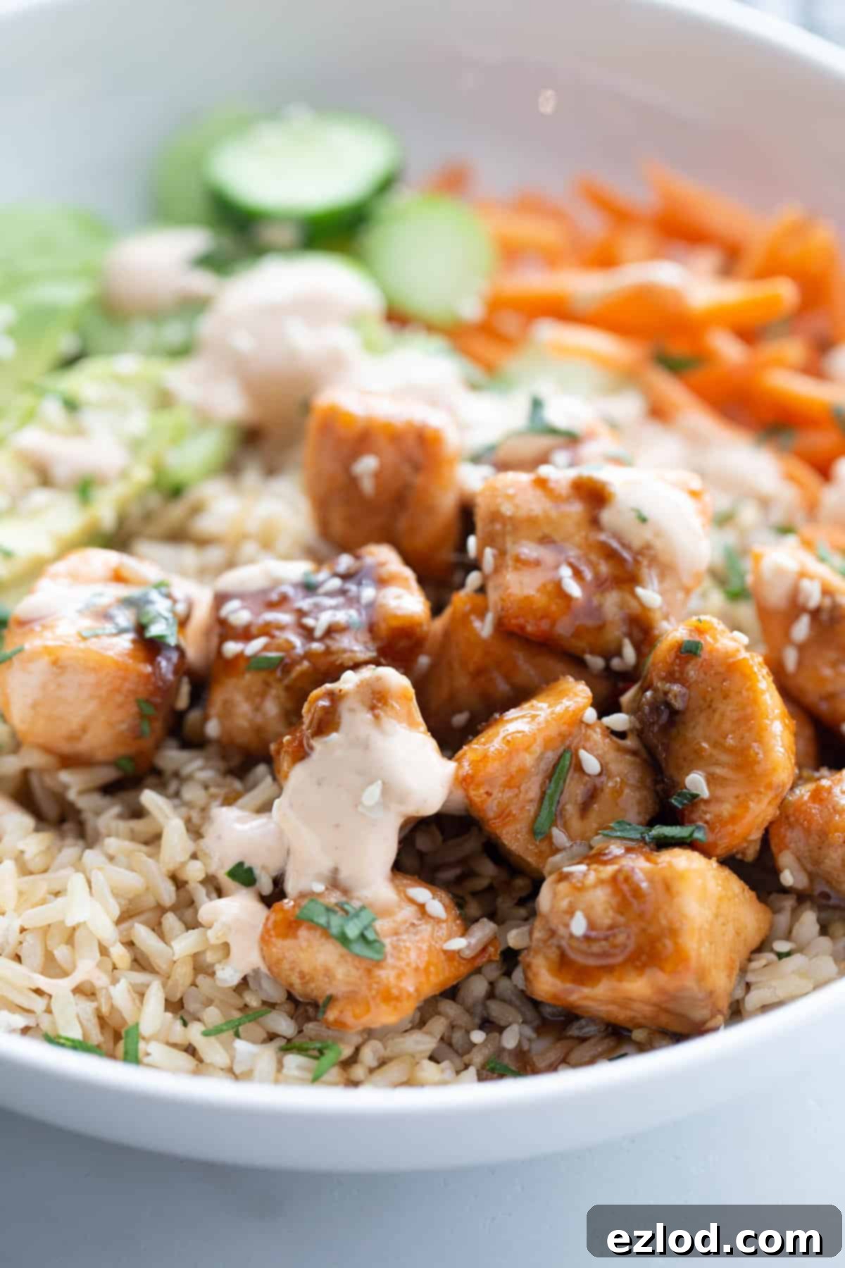 A close-up of a serving of sticky air fryer salmon bites over brown rice, garnished with spicy mayo, sesame seeds, and cilantro, highlighting the rich colors and textures of the dish.