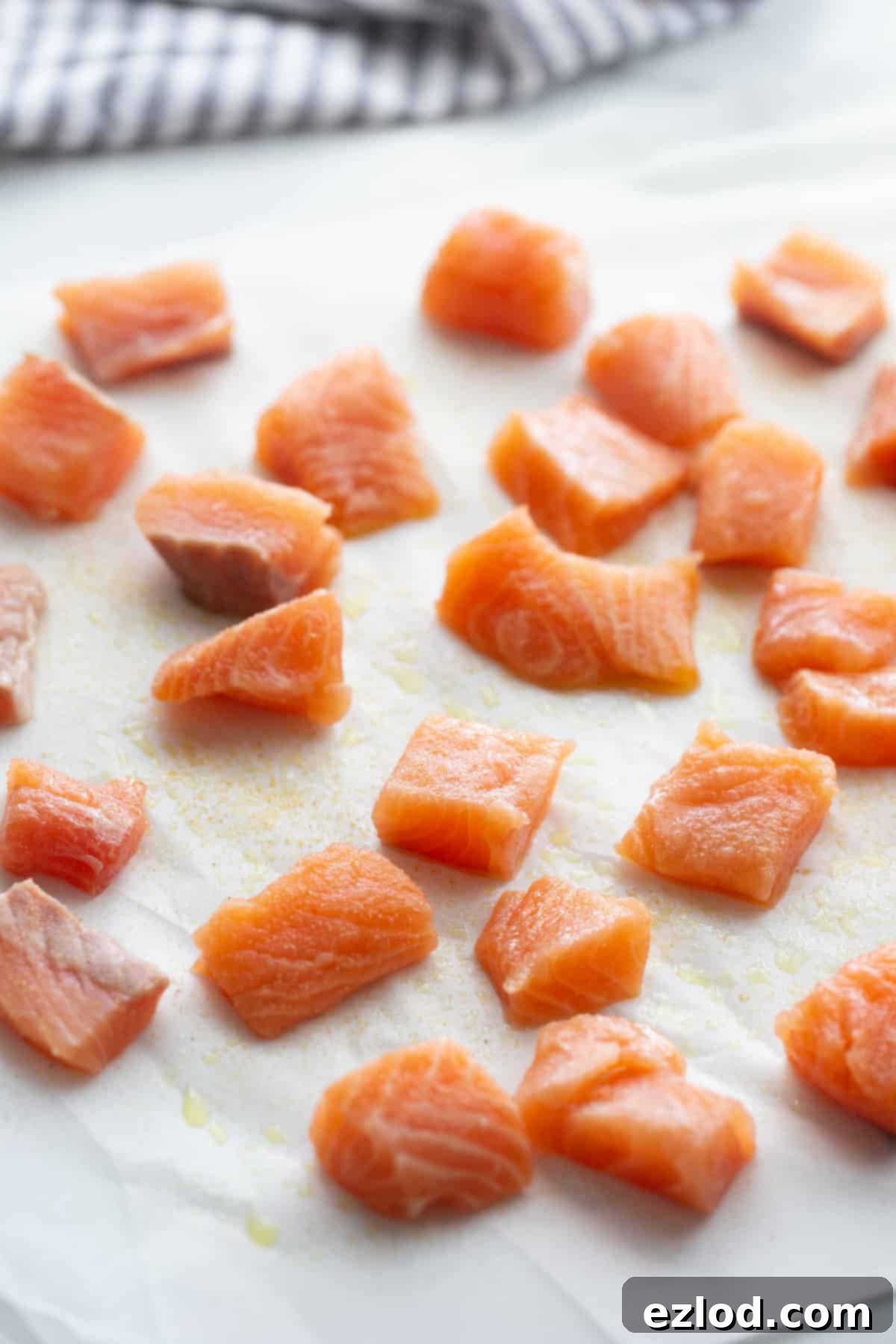 Seasoned cubes of fresh salmon ready for cooking, neatly arranged on a piece of parchment paper to prevent sticking and ensure even seasoning.