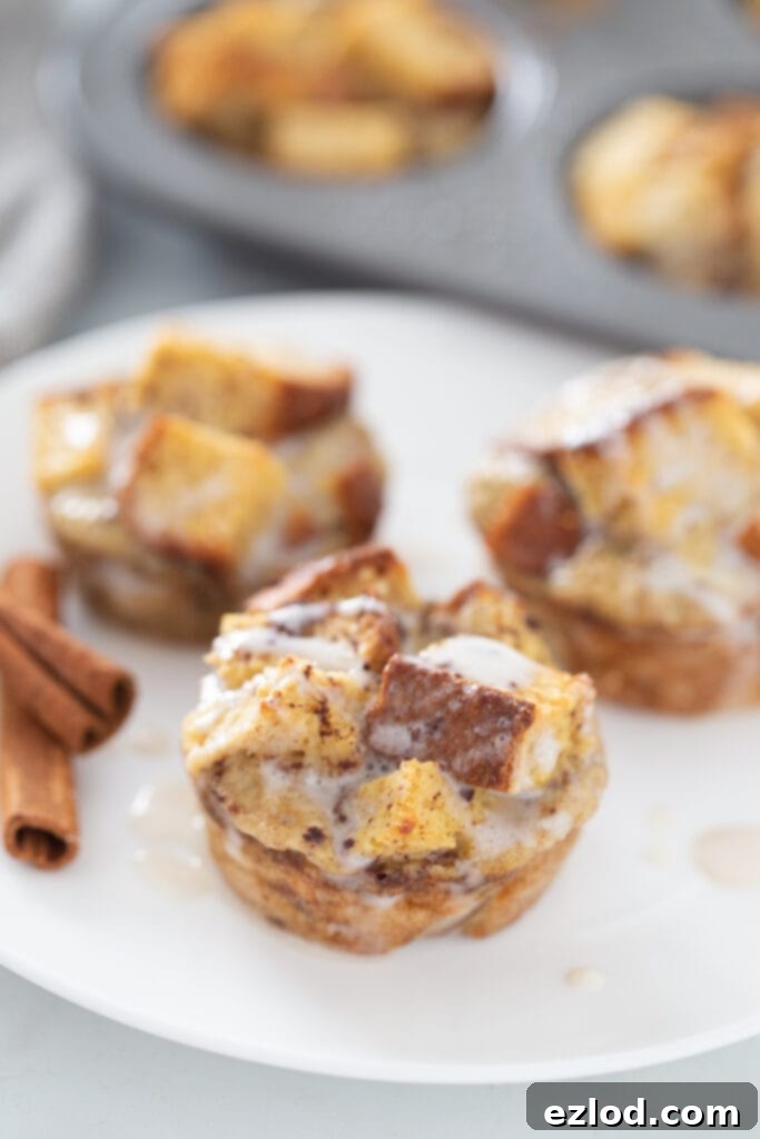 A close-up shot of three golden-brown French toast casserole muffins, lightly drizzled with white icing, sitting in a white muffin pan.