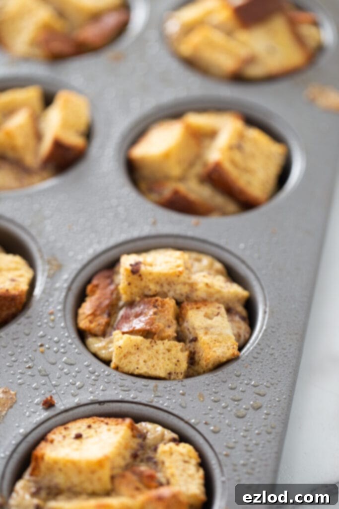 Freshly baked French toast cups, golden brown and perfectly risen, are cooling in a white cupcake tin.