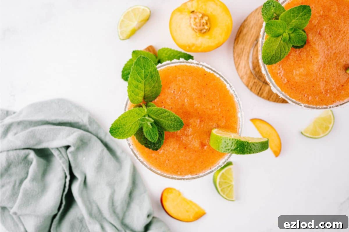 Top down shot of two frozen peach margaritas garnished with fresh mint, a lime wedge, and a salt rim.