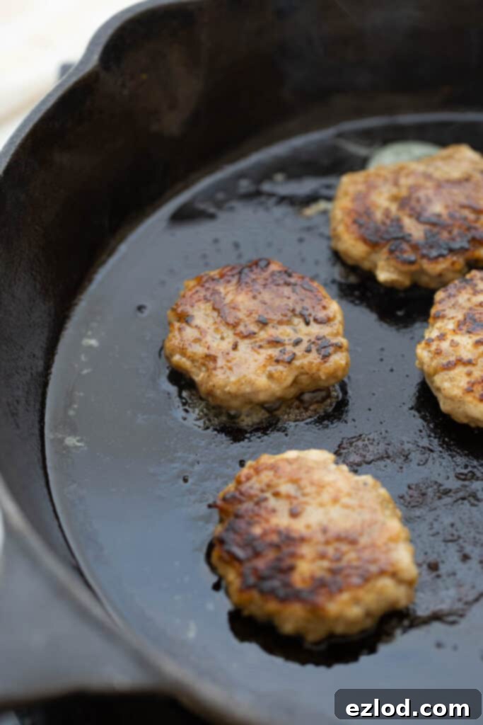 Homemade Maple Chicken Breakfast Sausages 7 Chicken breakfast sausage patties sizzling in a hot skillet, cooking to a golden brown.