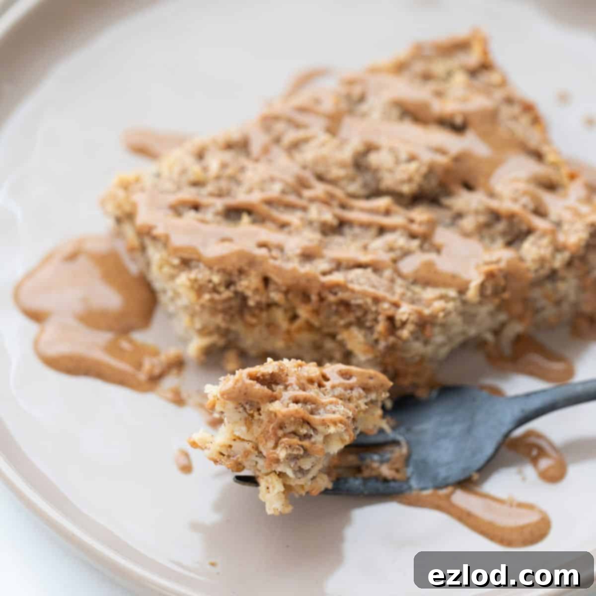 A piece of coffee cake baked oatmeal on a rimmed plate drizzled with peanut butter.