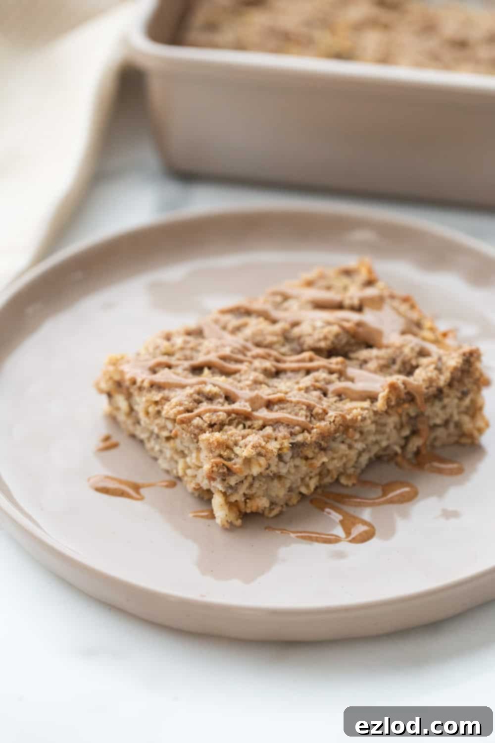 A piece of coffee cake baked oatmeal on a rimmed plate drizzled with peanut butter.