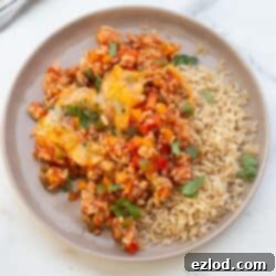 Unstuffed pepper skillet on a shite rimmed plate served with brown rice and garnished with fresh parsley.
