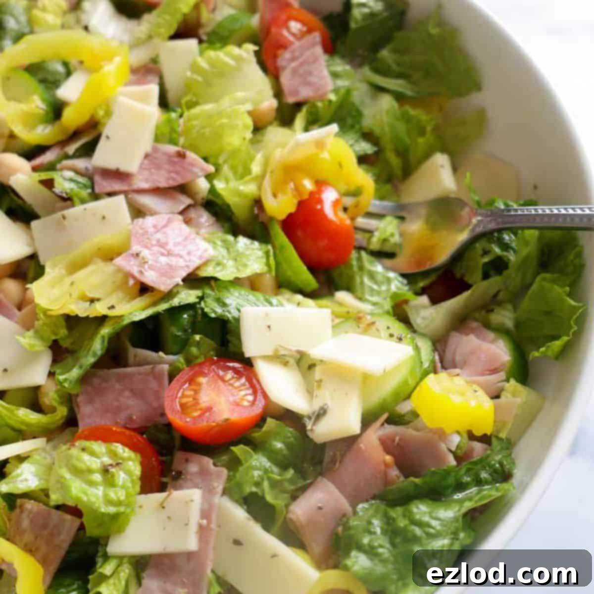 TikTok's Favorite Italian Grinder Chopped Salad 2 A vibrant bowl of Italian Chopped Grinder Salad featuring crisp lettuce, colorful tomatoes, cucumbers, and an assortment of deli meats, set on a white marble countertop.