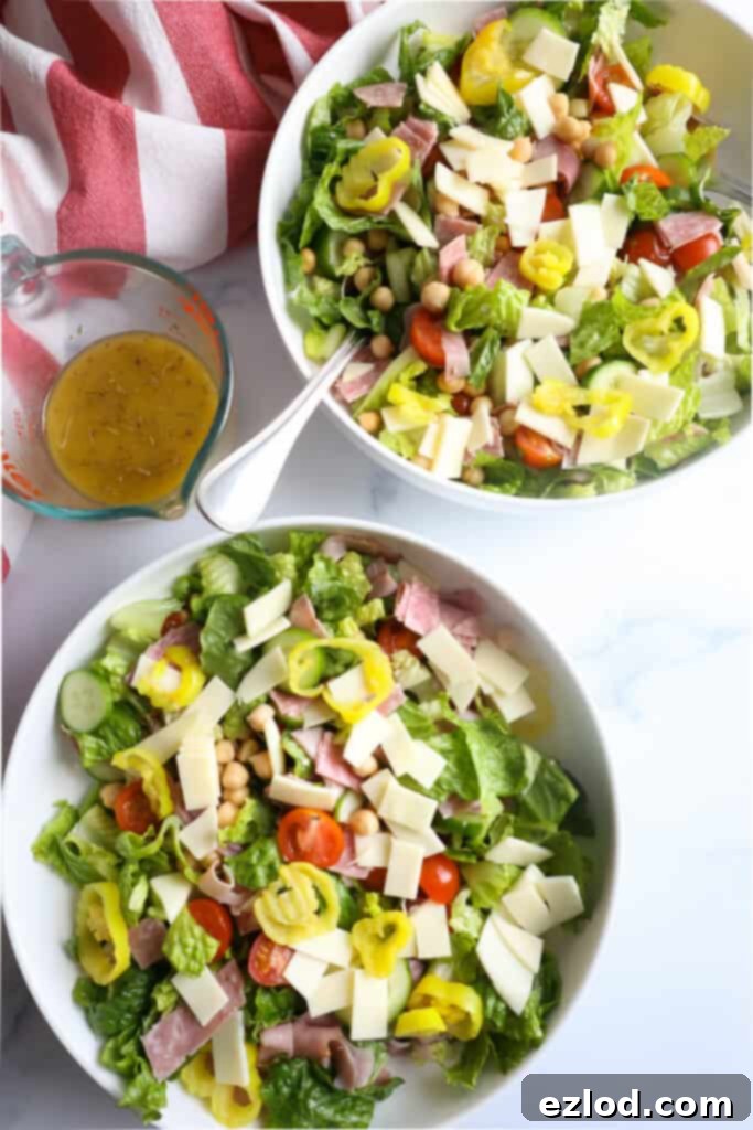 TikTok's Favorite Italian Grinder Chopped Salad 6 Two neatly arranged bowls of Italian Chopped Grinder Salad, garnished with banana peppers and provolone cheese, with the dressing in a separate small pitcher, ready to be served.